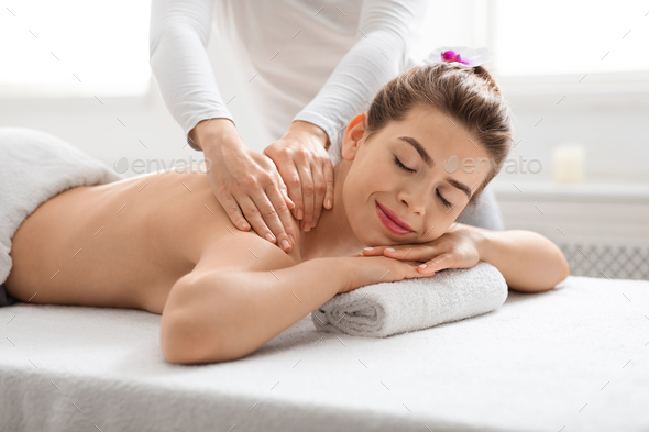 Joyful young lady getting back massage at spa Stock Photo by Prostock-studio