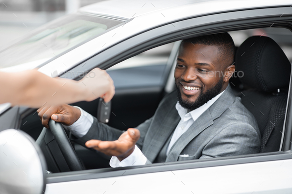 Excited african businessman sitting in new car, taking automatic key
