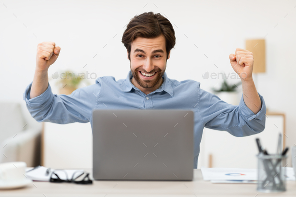 Man At Laptop Shaking Fists Celebrating Business Success In Office