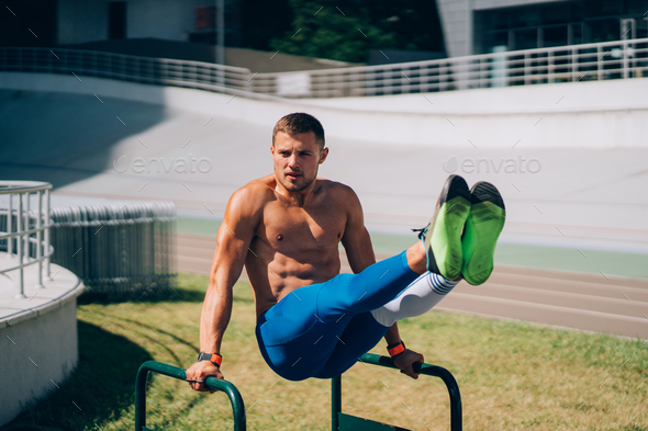 Strong man doing exercises on uneven bars in outdoor street gym