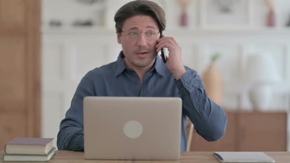 Young Man Talking on Phone while using Laptop in Office alt