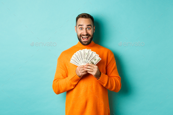 Image of excited bearded guy holding money and rejoicing, winning cash prize, standing against light