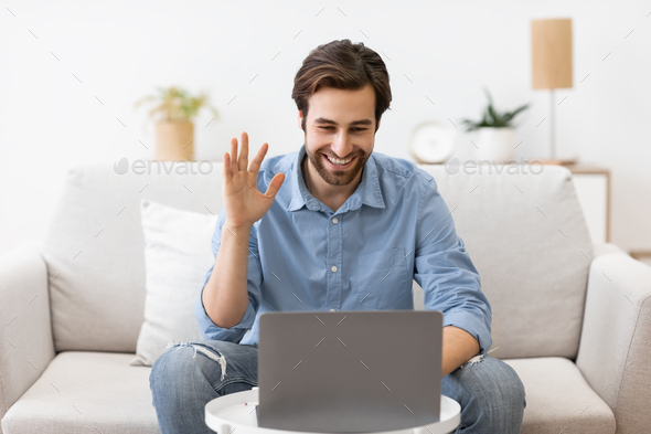 Man Waving To Laptop Making Video Call Sitting At Home