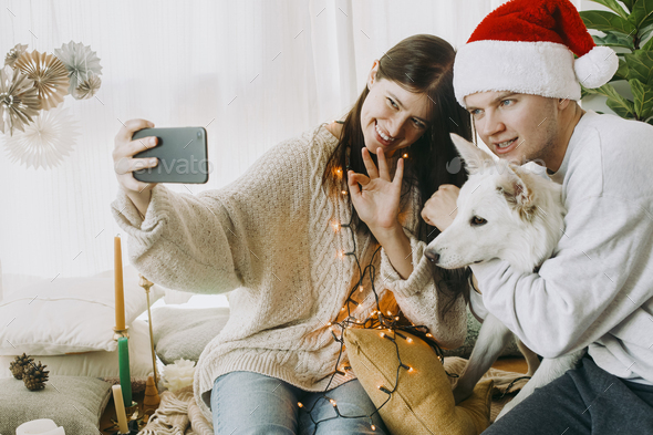 Happy family with cute dog waving hands in video call on phone, celebrating christmas online