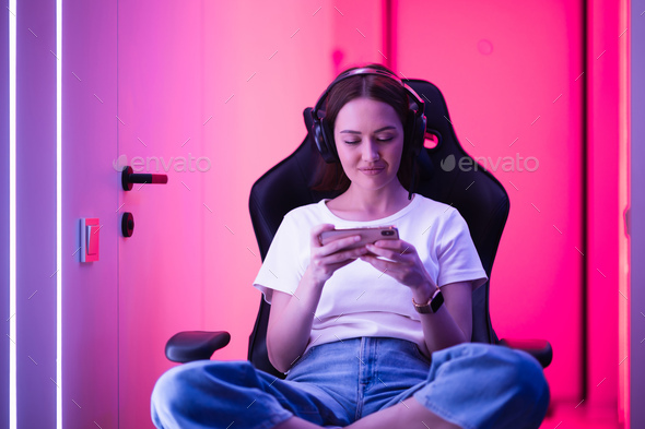 Cybersport gamer playing mobile game on the smart phone sitting on a gaming chair in neon color room