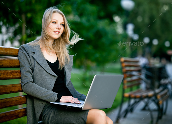 Businesswoman sitting on bench in park with notebook