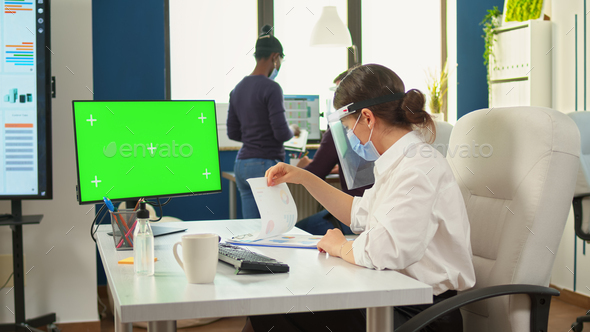 Manager with face mask typing on computer with green screen - Stock Photo - Images