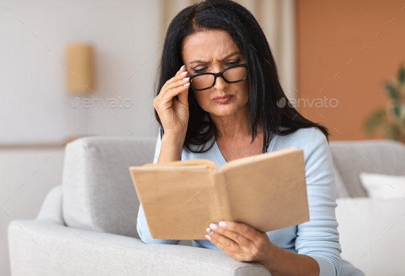 Mature woman touching glasses trying to read book