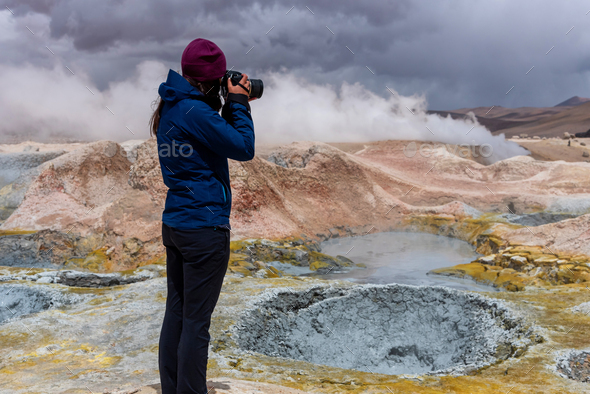 Woman with a camera photographing some mud pits with volcanic activity in the Andean Highlands