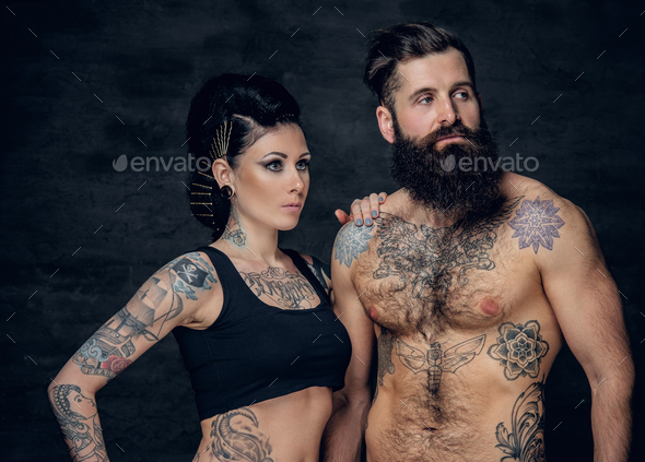 Studio portrait of full body tattooed couple over dark grey background.