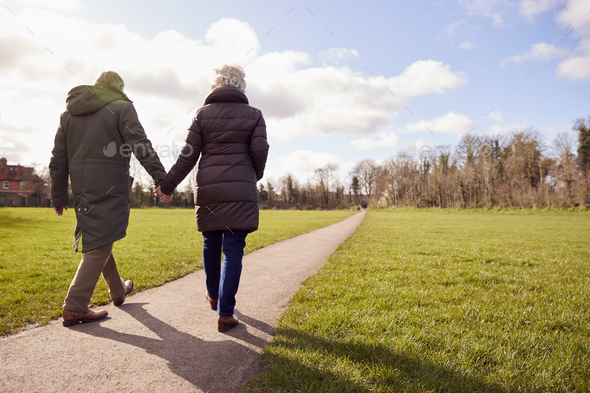 Rear View Of Loving Senior Couple Holding Hands Enjoying Autumn Or Winter Walk Through Park Together - Stock Photo - Images