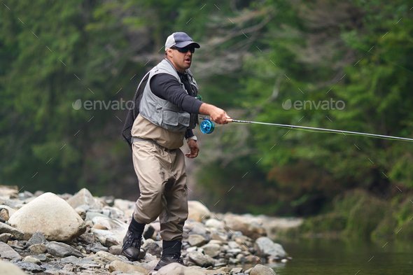 Fishermen in waterproof outfit fishing with rod Stock Photo by