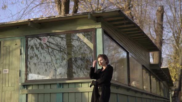 Portrait of Mused Brunette Stands at House with Crossed Hands alt