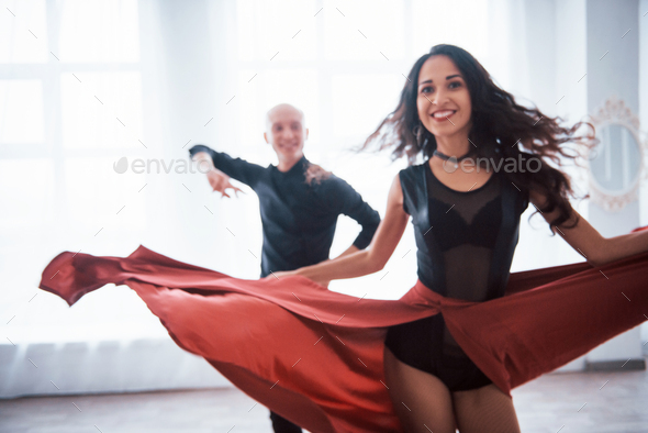 Young pretty woman in red and black clothes dancing with bald guy in the white room