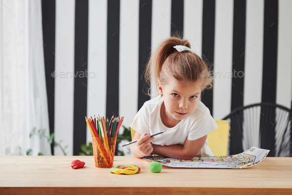 Cute little girl in art school draws her first paintings by pencils and markers