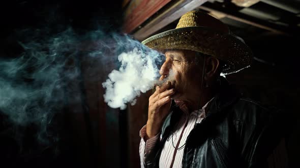 The man smokes a cigar. An elderly farmer in a straw hat smokes a cigar outside the ranch