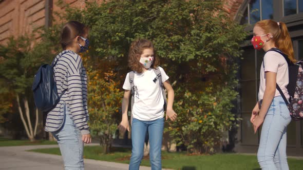 Three Schoolgirls in Safety Mask Bumping Elbows As Greeting Standing Outdoors alt