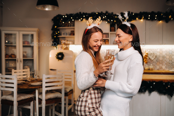 two girls in a cozy home environment with champagne in their hands at Christmas. Smiling girls drink