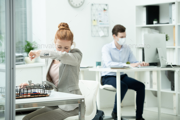 Young female office manager in suit and protective mask going to sneeze