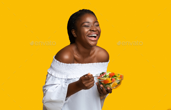 Laughing Black Woman Eating Healthy Vegetable Salad, Standing Over Yellow Background