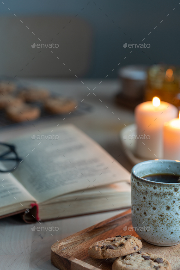 Reading book on cozy winter evening with candles, tea and cookies