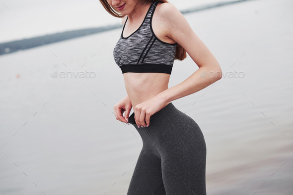 Holds pants by hands. Cropped photo of fitness girl posing after morning run near the lake
