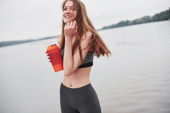 Satisfied sport woman. Photo of fitness girl have a rest after morning run near the lake