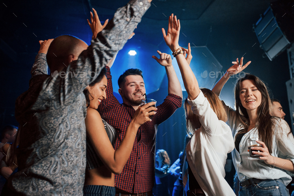 Happy people dancing in the luxury night club together with different drinks in their hands