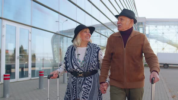 Elderly Husband Wife Retirees Tourists Go to Airport Terminal for Boarding with Luggage on Wheels alt