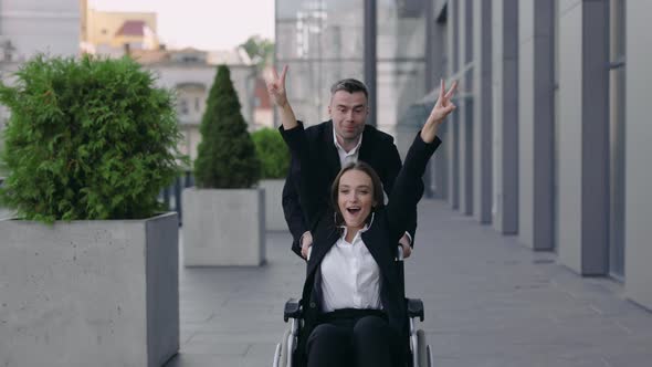 Crop View of Man Pushing Wheelchair with His Disabled Colleague and Smiling Near Office Building alt