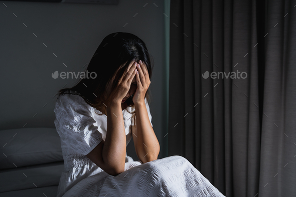 Lonely young woman feeling depressed and stressed sitting in the dark bedroom