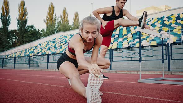 Closeup of a Girl and a Guy Stretch Their Leg Muscles Before an Outside Workout alt