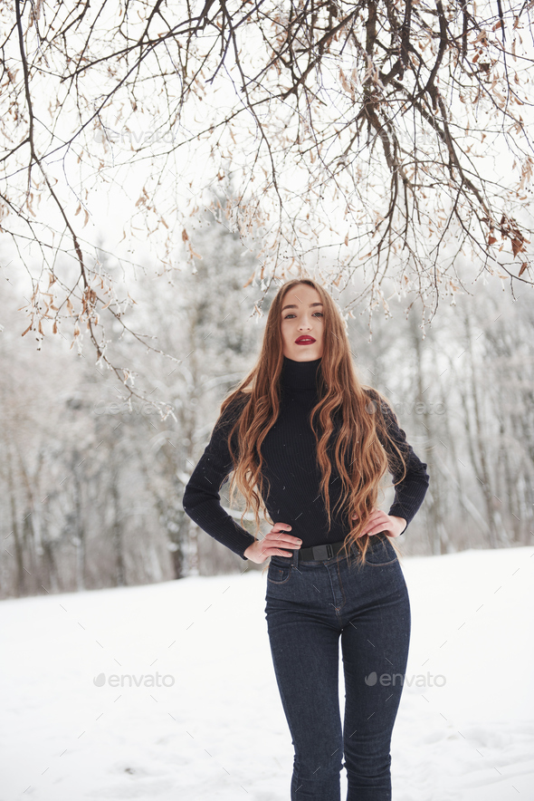 Hot modern woman. Pretty girl with long hair and in black blouse is in the winter forest