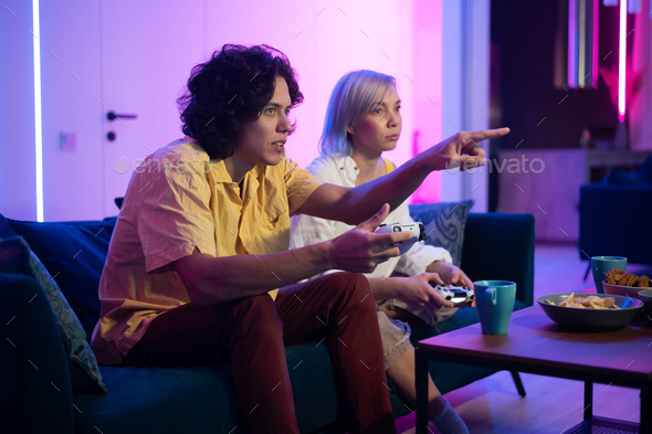 Handsome young man teaching how to play the video games to his girlfriend, on the couch, concept