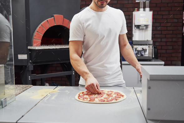 Baker in white shirt putting sausage rings to make delicious pizza for an order in restaurant