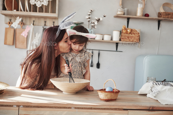 Mother and daughter in bunny ears at easter time have some fun in the kitchen at daytime