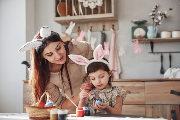 Mother and daughter in bunny ears at easter time have some fun in the kitchen at daytime