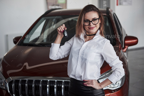It\'s yours now. Woman in eyewear and white shirt stands near the red automobile