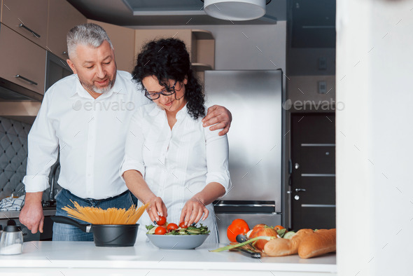 Man and his wife in white shirt preparing food on the kitchen using vegetables