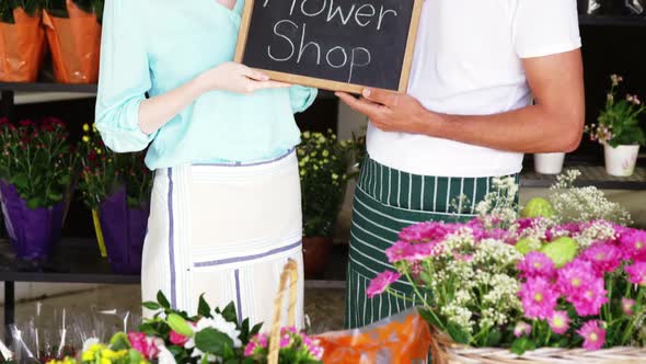 Smiling florists holding flower shop sign on slate in flower shop alt