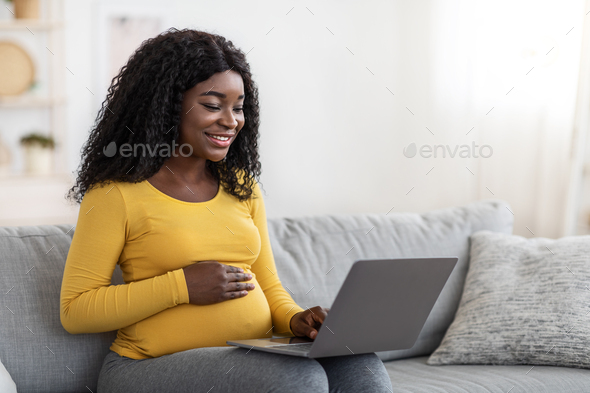 Smiling black pregnant lady using laptop at home