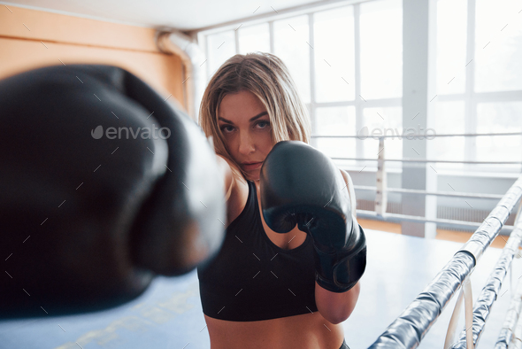 Punch in the face. Female sportswoman training in the boxing ring. In black colored clothes