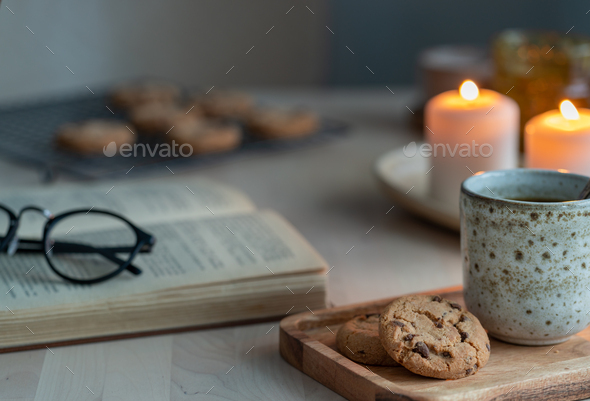 Reading book on cozy winter evening with candles, tea and cookies