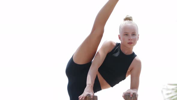 A Young Blonde Woman Gymnast Doing Stretching Exercises on the Open Sports Ground Using High Stands alt