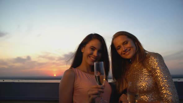 Cheerful Women With Glasses of Champagne Posing at Camera at Terrace on Sunset