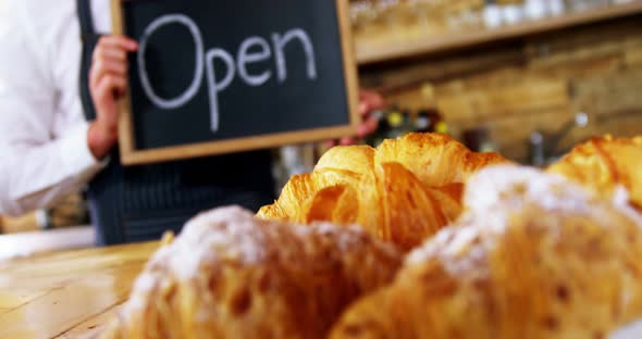 Smiling waiter holding open sign board alt