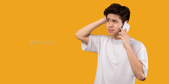 Confused asian man talking on mobile phone at studio