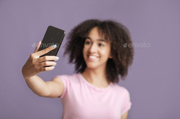 Happy lady makes selfie, focus on phone, isolated on violet background