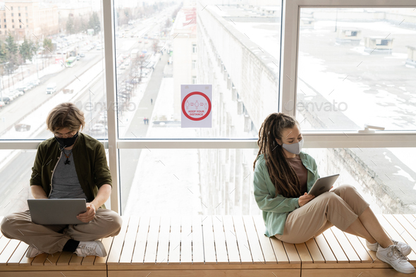 Two office workers sitting by window with announcement about keeping distance