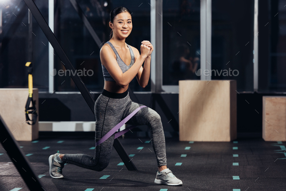 smiling asian girl doing lunges with rubber resistance bands at gym